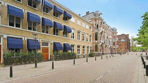 Une rangée de bâtiments de style européen traditionnel, tous dotés d’auvents uniformes au-dessus des fenêtres, une rue pavée et un ciel dégagé.