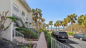 A residential building with a paved walkway, palm trees, and parked cars. - Gulf Views & Cozy Comfort w Large Lanai Tern's Nest #22 Condo by RVA (Longboat Key)