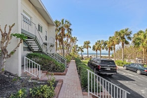 A residential building with a paved walkway, palm trees, and parked cars. - Gulf Views & Cozy Comfort w Large Lanai Tern's Nest #22 Condo by RVA (Longboat Key)