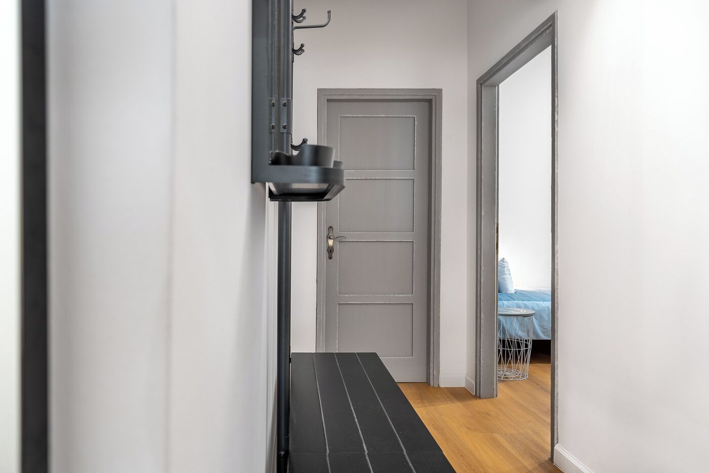 A hallway with a grey door, a black bench, and a metal rack with items.