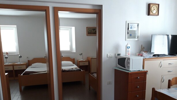 A compact room with two beds, a desk, a microwave, and a small kitchenette. - Apartmani Igor (Koper)