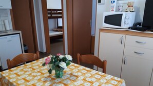 A dining area with a table covered in a floral tablecloth, wooden chairs, a vase with flowers, a microwave, and a small refrigerator. - Apartmani Igor (Koper)