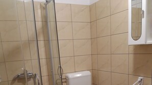 A bathroom with a shower, toilet, sink, and a patterned rug. - Apartmani Igor (Koper)