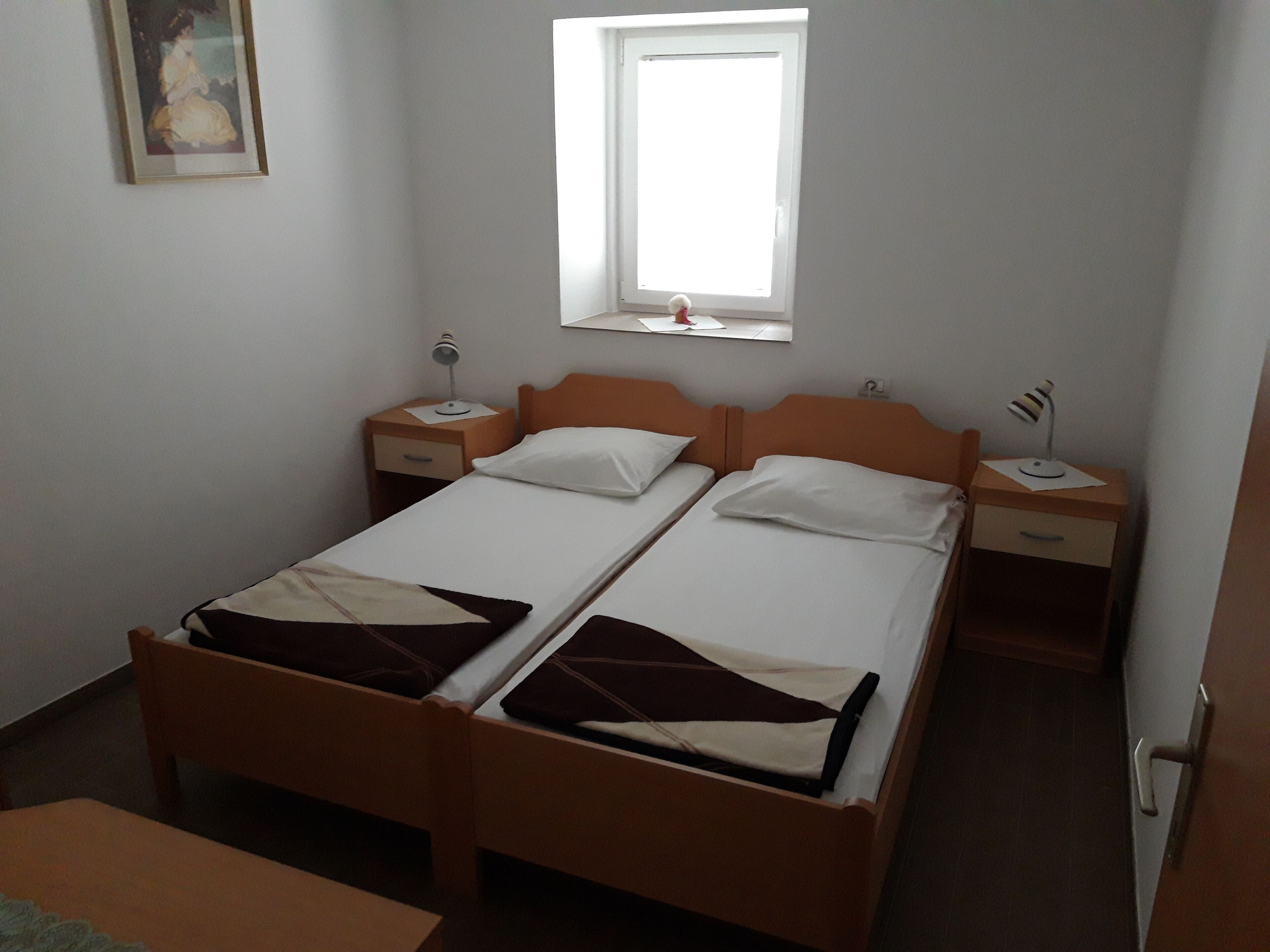 A twin room with two single beds, a small desk, a nightstand, a window, and a painting on the wall.