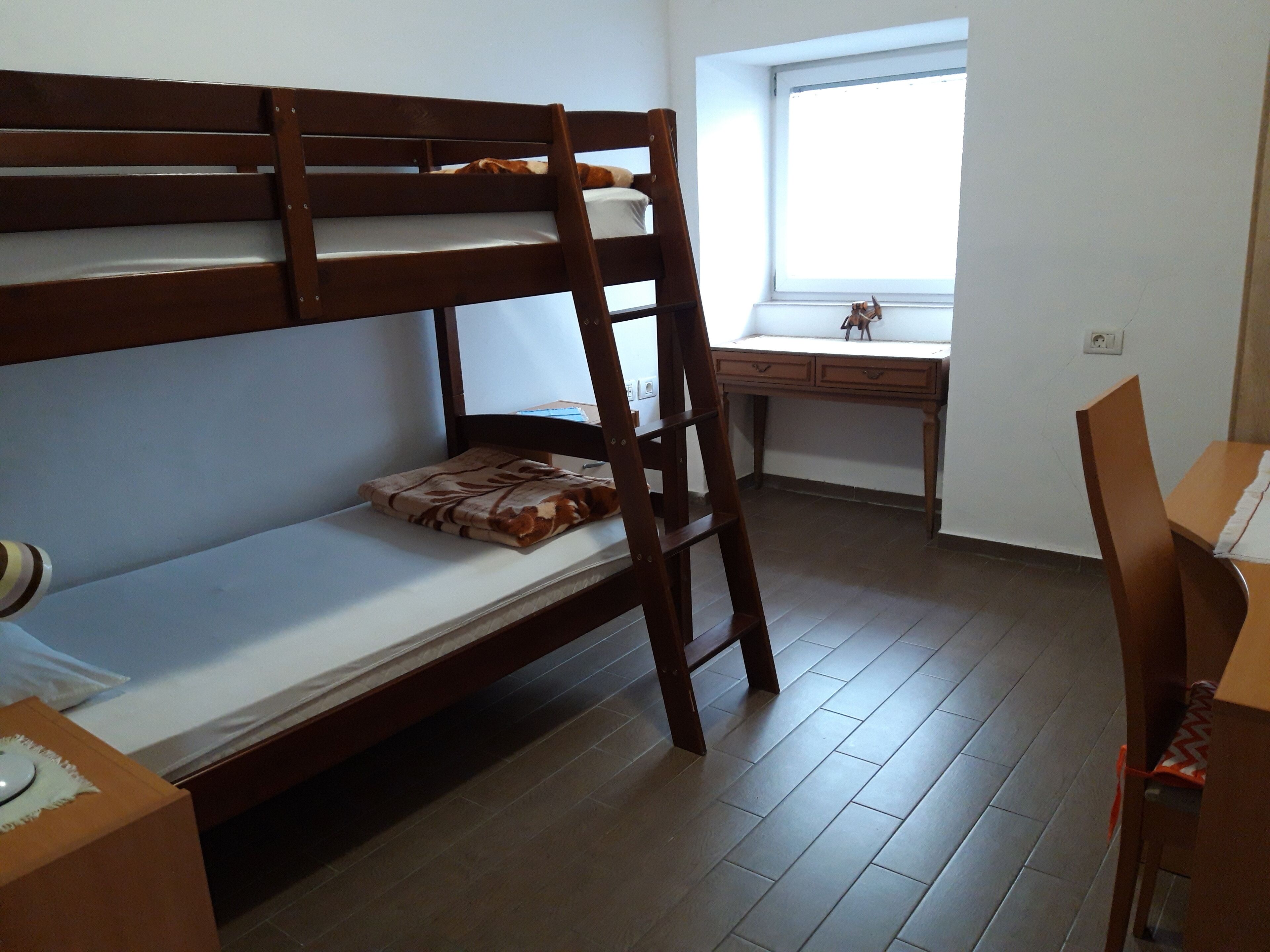 Un letto a castello con una scrivania e una sedia, una finestra e un tavolino con una lampada.