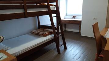 A bunk bed with a desk and chair, a window, and a small table with a lamp.