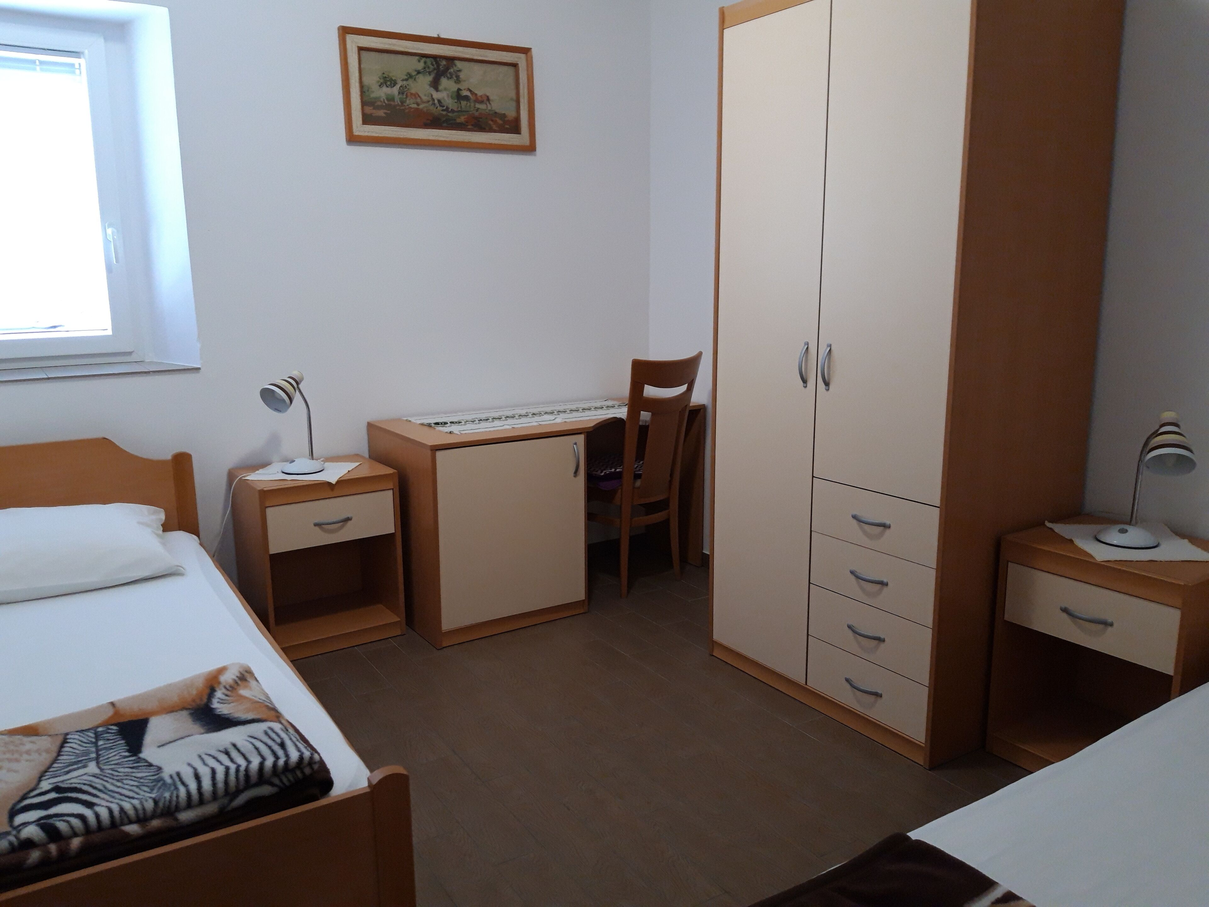 A bedroom with a bed, a desk, a chair, a wardrobe, and a window.