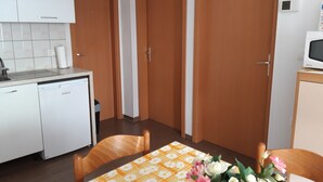 A compact kitchen with a dishwasher, a small sink, and a microwave on a cabinet. There are two wooden doors and a table with a floral tablecloth. - Apartmani Igor (Koper)