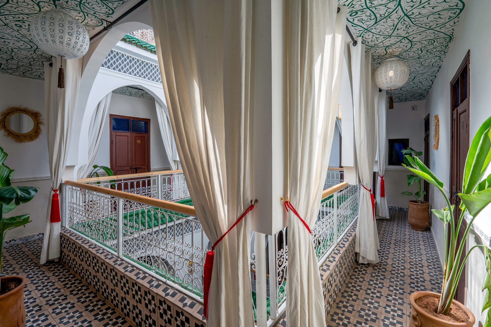 Un interior tradicional marroquí con patio, techo ornamentado y balcón con baranda de metal.