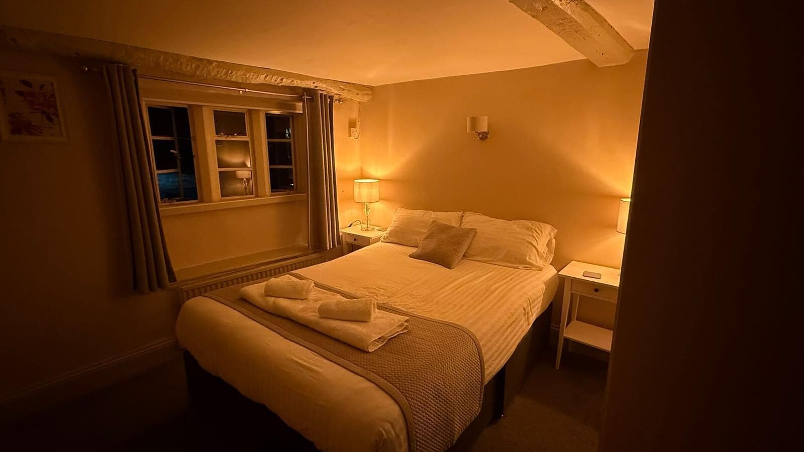 Une chambre d’hôtel avec un lit, des tables de chevet, une lampe et une fenêtre avec des rideaux.