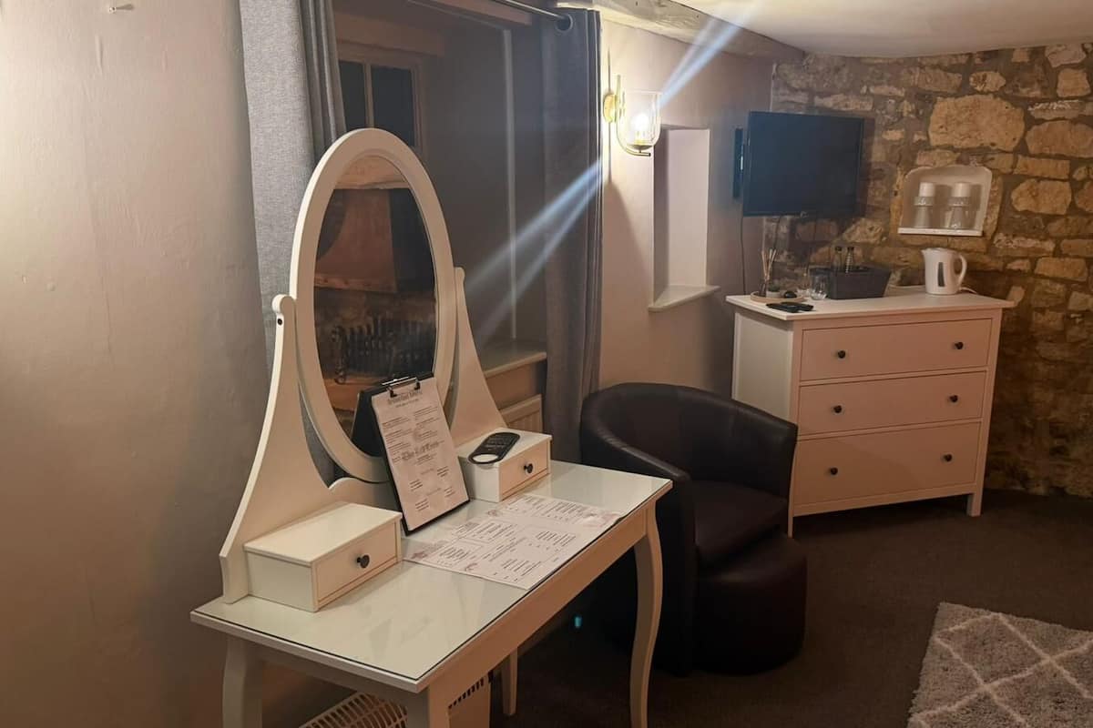 Quarto com toucador, espelho, secretária, cadeira, cómoda, televisão e paredes de pedra.