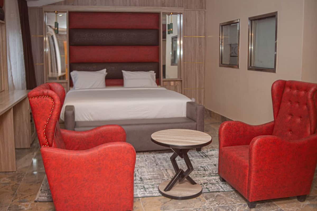 Ein Hotelzimmer mit einem großen Bett, zwei roten Sessel, einem kleinen runden Tisch und einem Spiegel an der Wand.