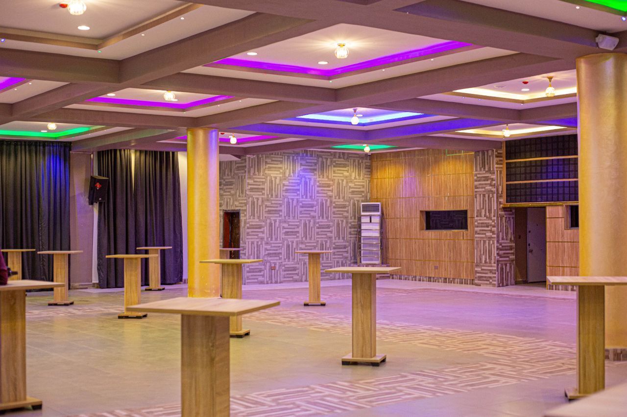 Un amplio salón con paredes decoradas, mesas de madera y luces en el techo.
