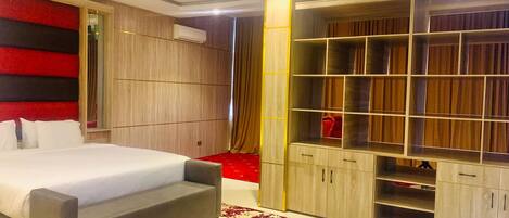 A modern bedroom with a large bed, built-in wardrobe, and a red accent wall.