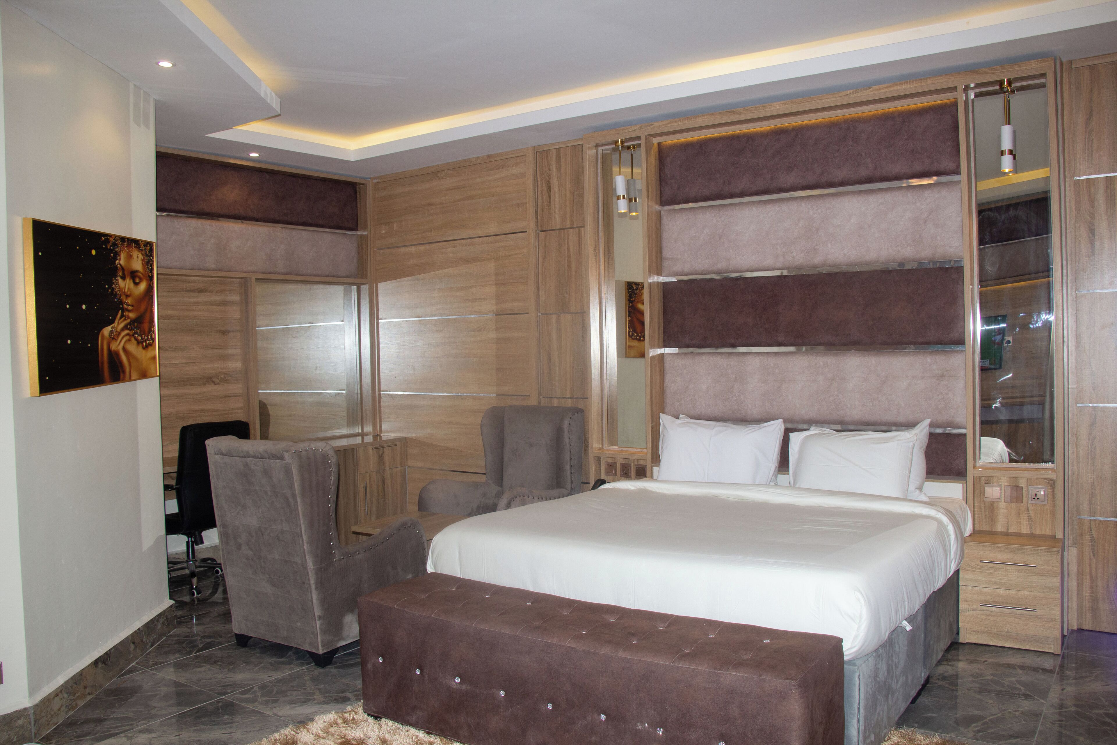 A modern bedroom with a large bed, a seating area with chairs, and a built-in wardrobe.