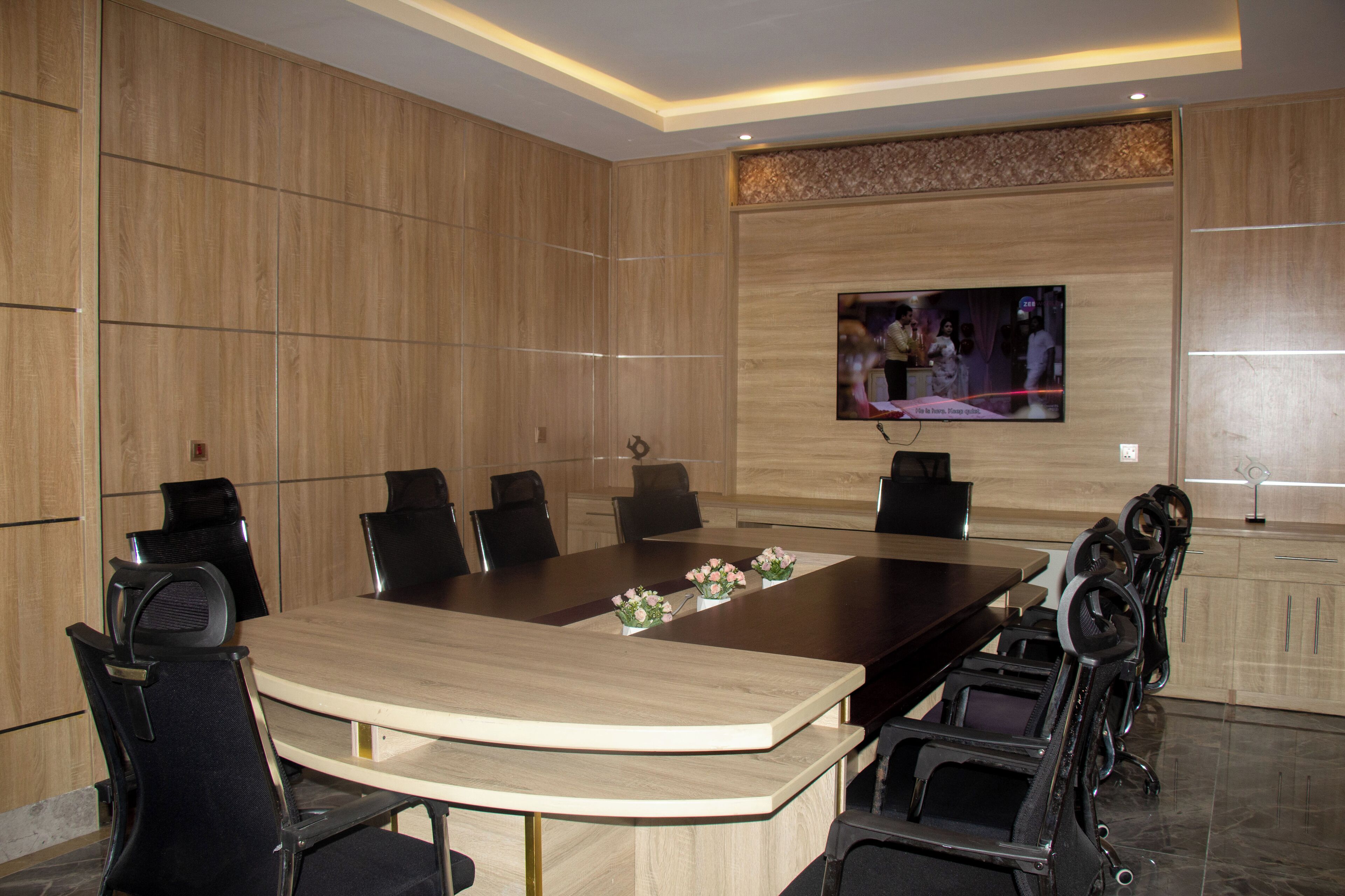 A conference room with a large table, black chairs, and a mounted TV on the wall.
