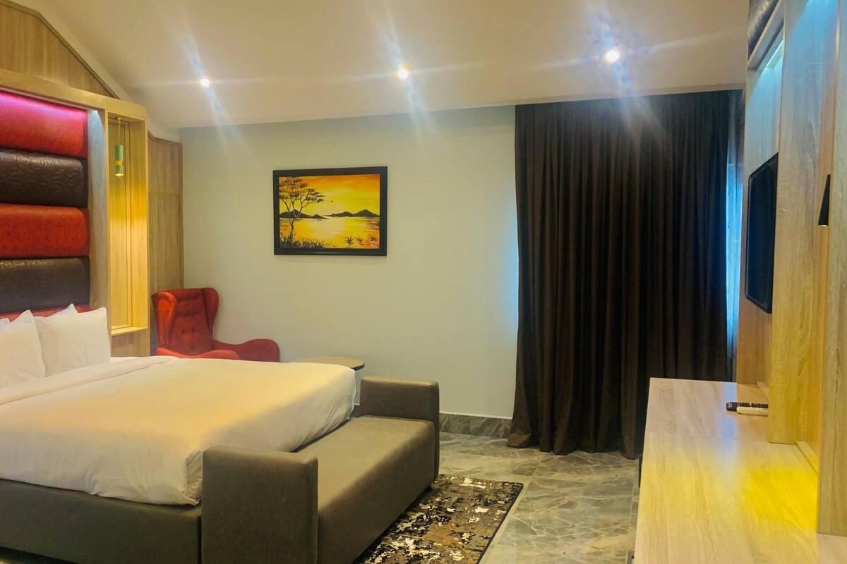 Ein modernes Hotelzimmer mit einem großen Bett, einem roten Sessel, einem kleinen Tisch und einem Gemälde an der Wand.