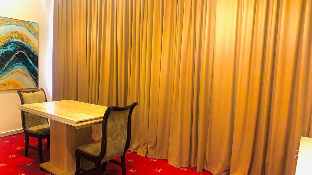 Une pièce avec une table en bois et deux chaises, une moquette rouge et un grand rideau.