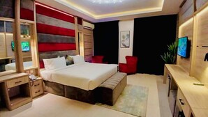 A modern bedroom with a large bed, bedside tables, a TV, and a ceiling light fixture. - Ceedapeg Hotels (Uyo)