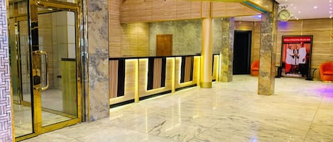 A hotel lobby with marble flooring, a reception desk with illuminated panels, and a poster promoting unity.