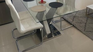 Un espace repas moderne avec une table à plateau en verre, des chaises blanches à coussin et un tableau accroché au mur.