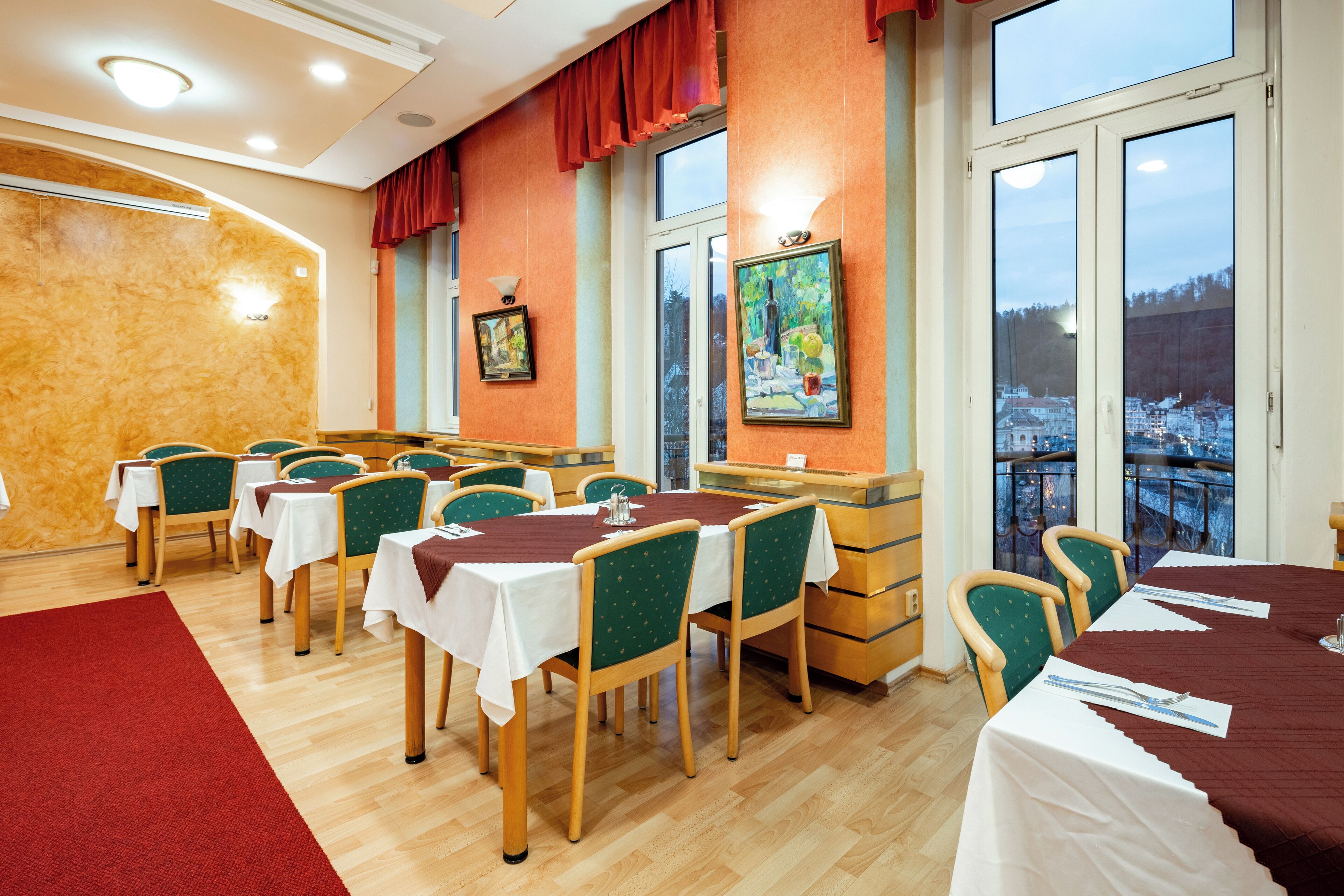 A dining area with multiple tables and chairs, large windows with a view, and a red carpet.