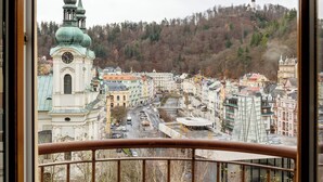 A cityscape with historic architecture, including a prominent church with a clock tower and a hill with a castle-like structure in the background. - Wellness hotel Jean de Carro (Karlovy Vary)