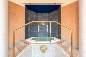 Un área de spa con jacuzzi, suelo de mármol y barandilla dorada.