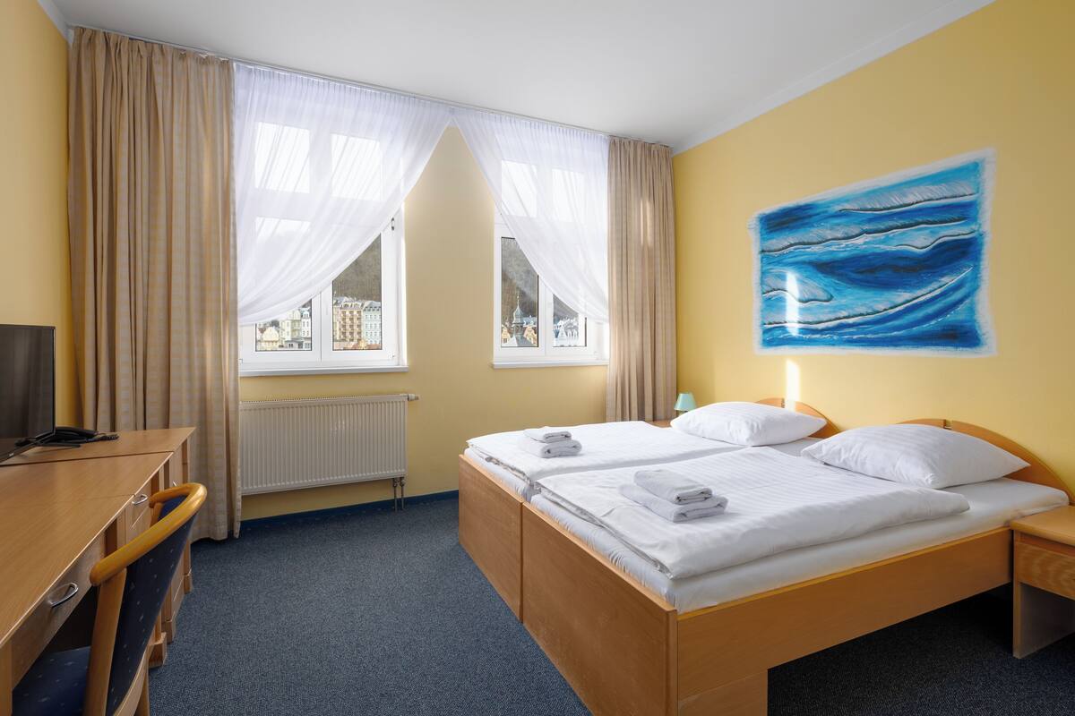A hotel room with two beds, a desk, and a window with curtains.