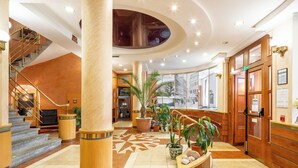 A hotel lobby with a grand staircase, a central column, and a check-in desk. - Wellness hotel Jean de Carro (Karlovy Vary)