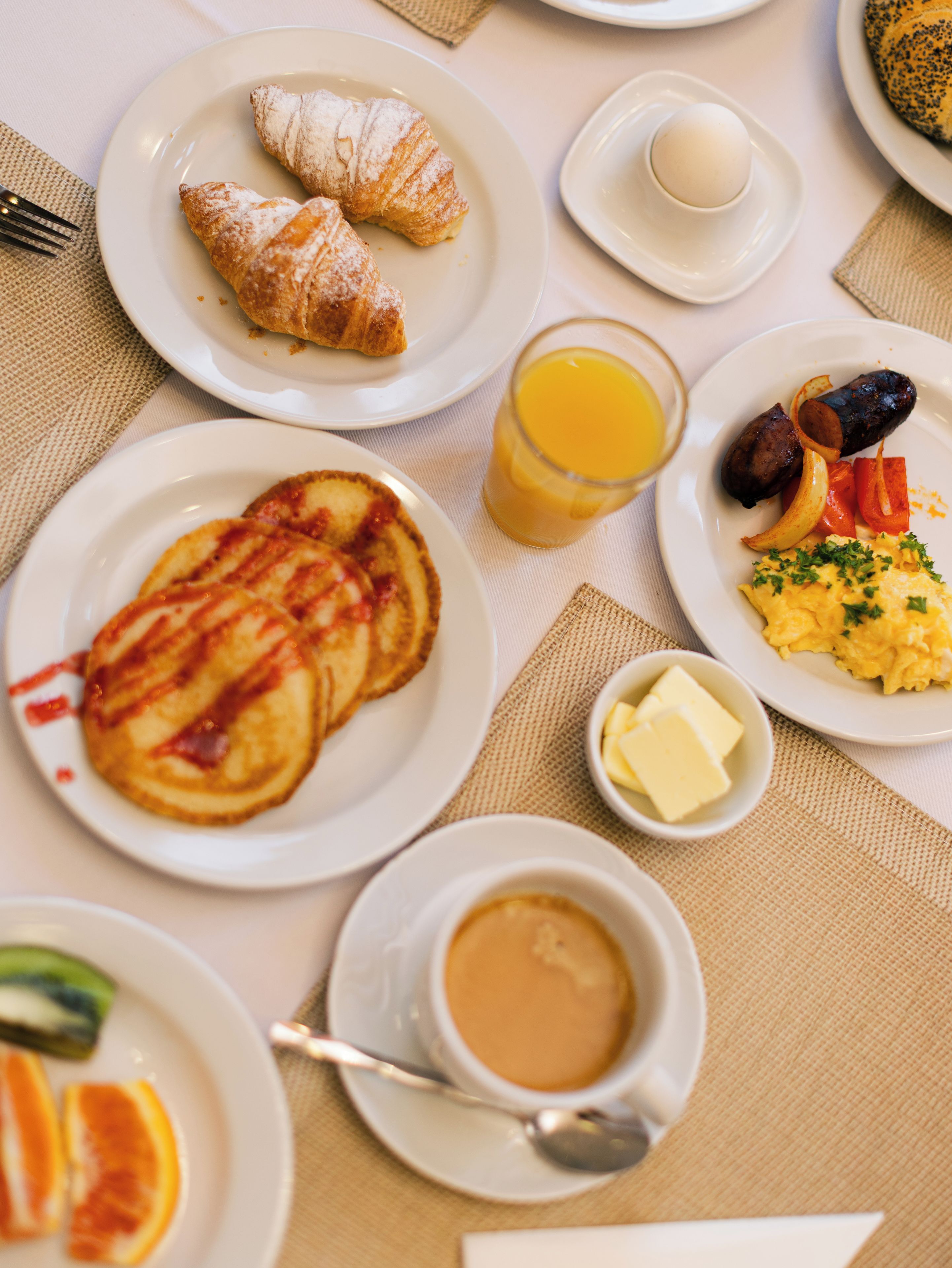 Ein gedeckter Frühstückstisch mit Speisen, einem Glas Orangensaft und einer Kaffeetasse.