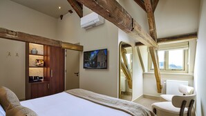 A bedroom with a large bed, a wooden wardrobe, a chair, and a painting on the wall. - The Saints Hotel ('s-Hertogenbosch)