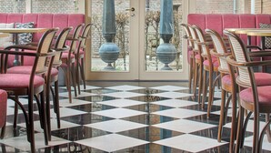 A restaurant with checkered flooring, red upholstered seating, and a large chandelier. - The Saints Hotel ('s-Hertogenbosch)