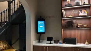 A reception area with a checkered floor, a staircase, a reception desk, and a wall-mounted television. - The Saints Hotel ('s-Hertogenbosch)