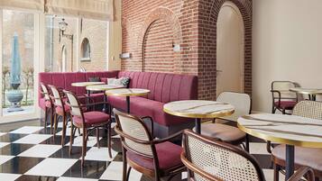 Un café avec un sol à carreaux, des sièges rembourrés de couleur rouge et des tables rondes.