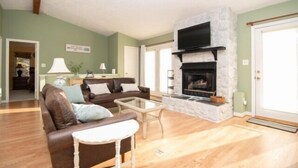 A living room with a stone fireplace, a brown leather sofa, a glass coffee table, and a television mounted above the fireplace. - Boats N Oats: Great family getaway, wifi, gentle lot, kayak (Moneta)