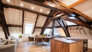 Ein geräumiger Loft mit hohen Decken, freiliegenden Holzbalken, einer zentralen Essecke mit Stühlen und Tisch, einer Küche mit einer Holzinsel und einem Sofa.