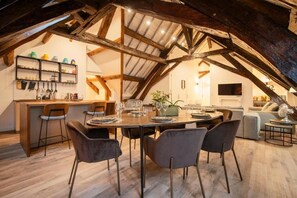 Un comedor con mesa y sillas de madera, una zona de bar con taburetes y una cocina al fondo.