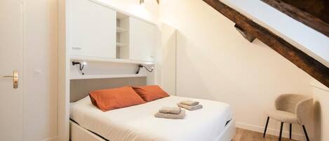 Une chambre à coucher avec un lit, une chaise et une armoire blanche.
