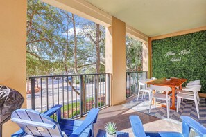 A balcony with a view of trees and a street, a wooden table with white chairs, and a green wall with text. - Spacious Hilton Head Island Condo - 1 block to Beach & 60+ shops/restaurants (Hilton Head Island)