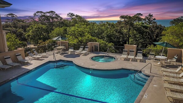 A pool area with lounge chairs and a hot tub, surrounded by trees and overlooking a body of water. - Spacious Hilton Head Island Condo - 1 block to Beach & 60+ shops/restaurants (Hilton Head Island)