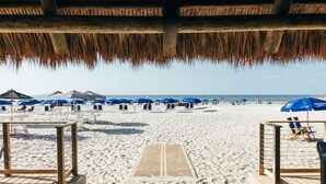 Ein Strand mit strohgedeckten Hütten und blauen Sonnenschirmen.