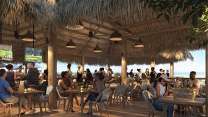 Ein Essbereich im Freien mit Reetdächern, Korbmöbeln und Blick auf den Strand.