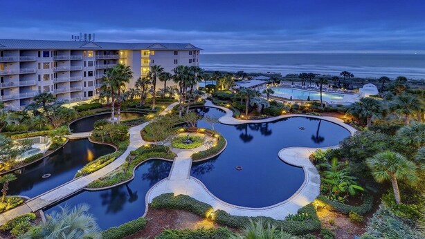 Ein Resort mit mehreren Schwimmbecken, einem großzügigen Gebäude mit Balkonen und Blick auf den Ozean.