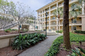 A multi-story hotel with a central courtyard, outdoor seating, and a staircase leading to the upper floors. - Spacious Hilton Head Island Condo - 1 block to Beach & 60+ shops/restaurants (Hilton Head Island)