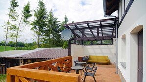 A covered outdoor patio with a wooden deck, a yellow sofa, and a satellite dish. - Apartment for two Only 20 m From Boruja Lake in Rekowo (Bytow)