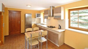 A compact kitchen with a built-in refrigerator, a microwave, and a gas stove. There is a dining area with a table and chairs. - Apartment for two Only 20 m From Boruja Lake in Rekowo (Bytow)