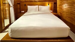 Una habitación con paneles de madera, una cama grande, una ventana con cortinas y una mesita de noche con lámpara.