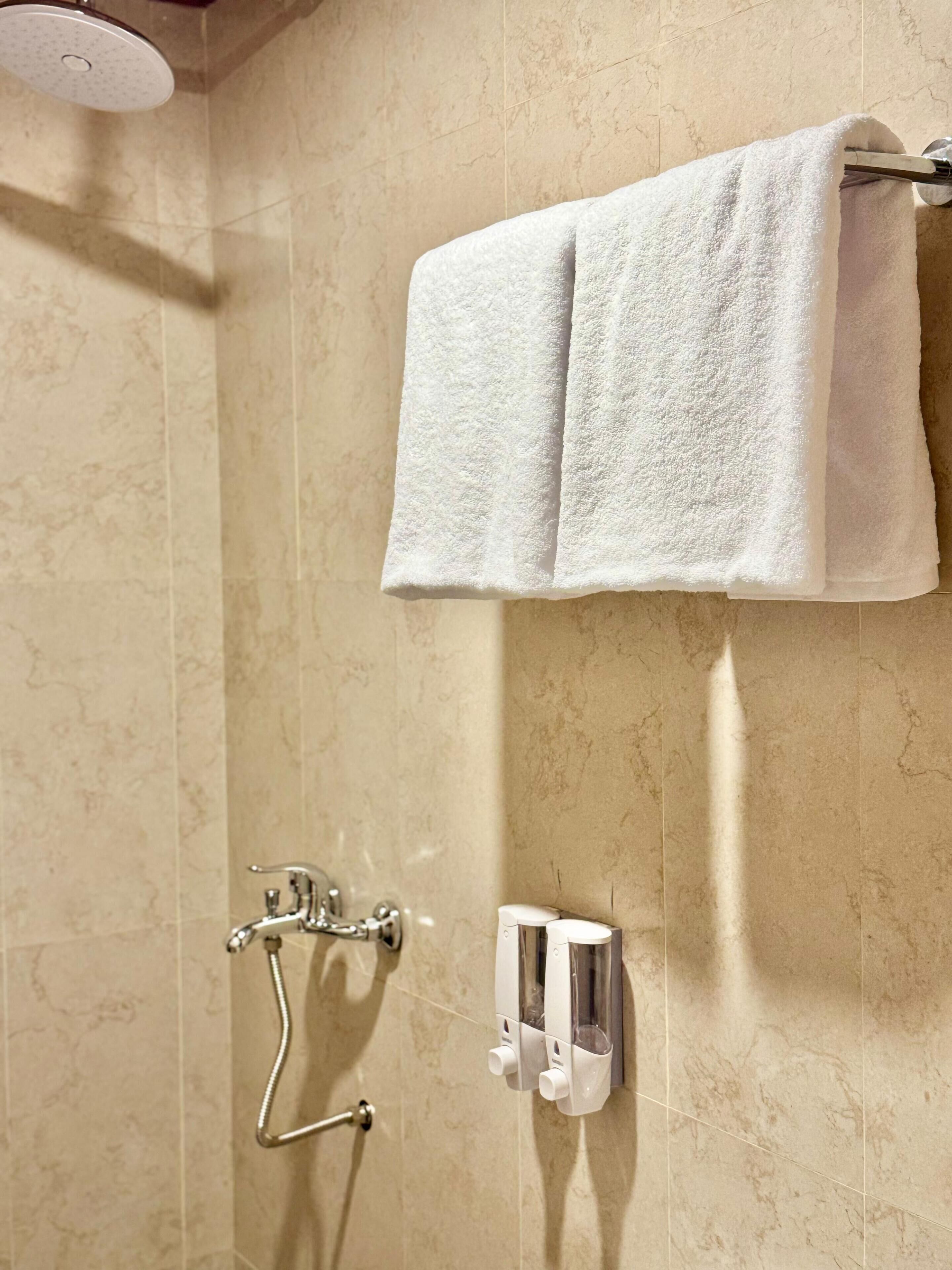 Un baño con ducha, un toallero con dos toallas, un cabezal de ducha manual y un dispensador de jabón.