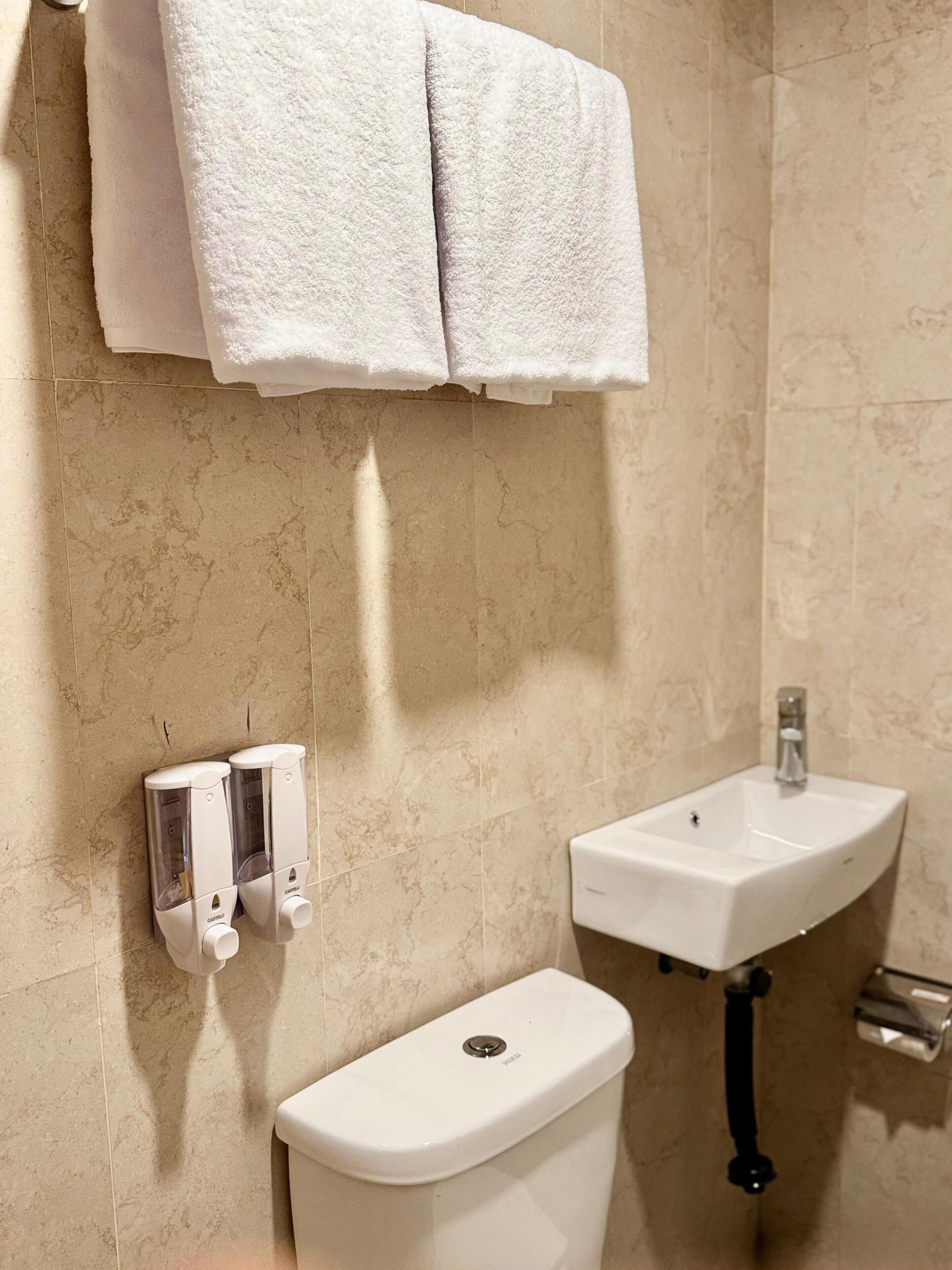 A bathroom with a toilet, a sink, and a hand sanitizer dispenser.